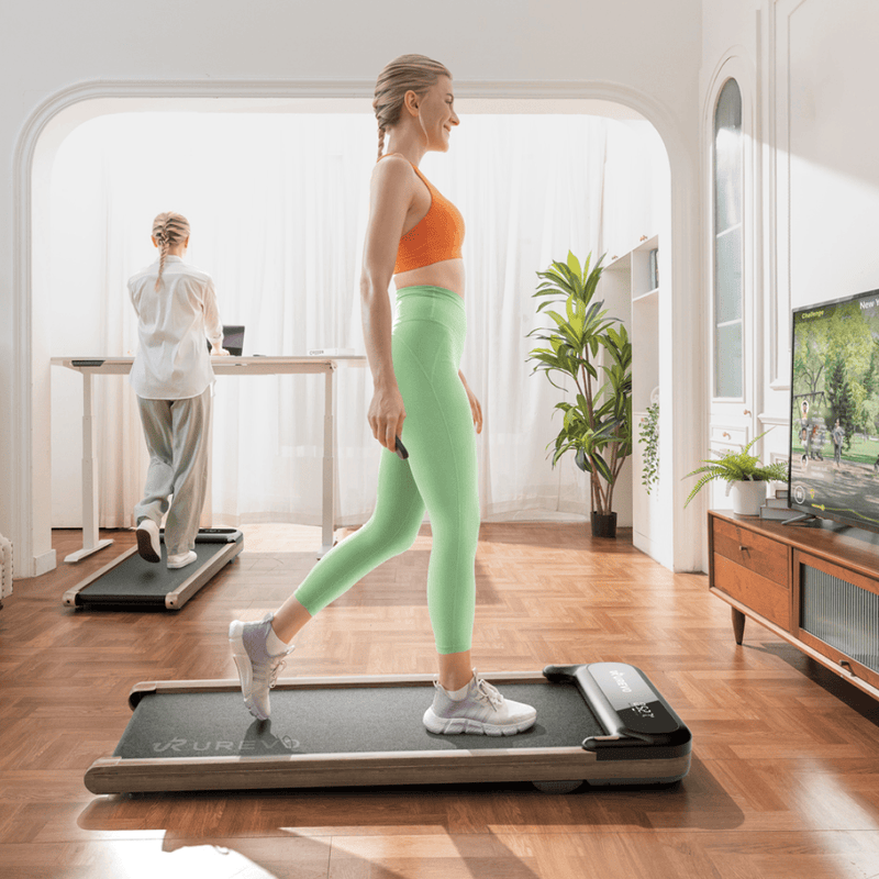 A woman in an orange top and green leggings walks on a treadmill in a bright