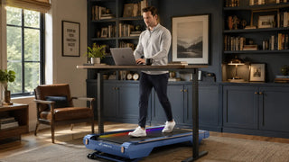 Man walking on a under-desk treadmill while working in a home office.