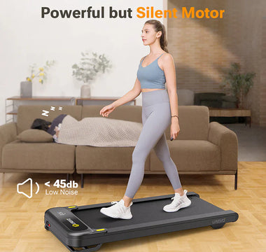 A woman walking on a treadmill in a living room, with a person sleeping on the couch behind her.