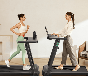 Two women use treadmills: one exercises in sportswear, while the other works on a laptop in casual attire.