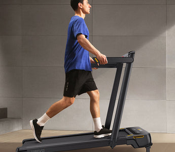 A man in a blue shirt and black shorts is walking on a treadmill.